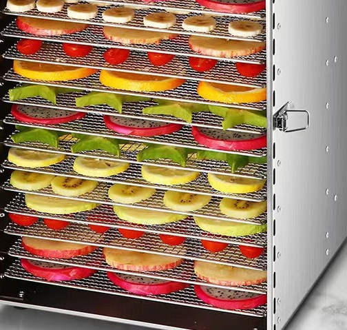 Open food dehydrator with stacked mesh trays holding sliced fruits and vegetables